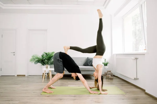 Beautiful sporty fit couple, young man and woman, practicing yoga together at home, doing paired gymnastic yoga asana exercises at home. Balance, meditation and yoga concept — Stock Photo, Image