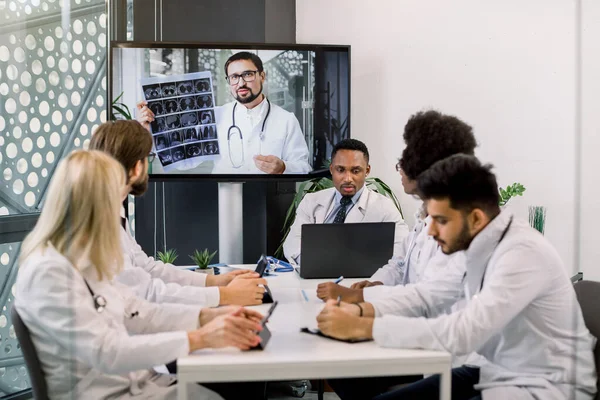 Çevrimiçi video konferansı, teletıp, sosyal mesafeler, webinar toplantısı. Çok ırklı doktorlardan oluşan bir ekip, tomografi taraması yapan deneyimli beyaz erkek doktorla video konferansında. — Stok fotoğraf