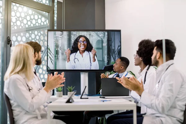 Videokonference, telemedicína. Multietnický lékařský vědecký tým tleskající během videokonference se svou africkou kolegyní, vyjadřující své vzrušení zaťatými pěstmi — Stock fotografie
