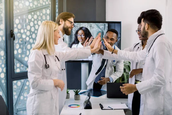 Concetto di telemedicina, sanità e lavoro di squadra. Gruppo multietnico di medici che si riuniscono in videoconferenza con la loro giovane collega africana, dando il cinque per celebrare il successo — Foto Stock