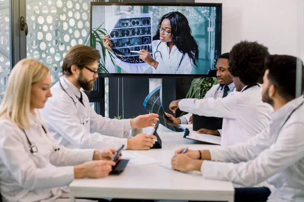 Team di medici o scienziati esperti multirazziali, che tengono videoconferenze con la loro giovane esperta africana fiduciosa e parlano dei risultati della TC dei pazienti durante la sperimentazione clinica — Foto Stock