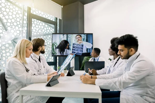 Vue de face de cinq médecins multiraciaux confiants discutant du plan de traitement du patient lors d'une vidéoconférence avec leurs collègues afro-caucasiens et caucasiens. Télémédecine, chat vidéo — Photo