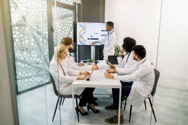 Yakışıklı Afrikalı doktor büyük dijital ekran ve çizelgeler kullanarak, çok ırklı meslektaşları için bir ders raporu hazırlarken, yeni bilimsel araştırmasının sonuçlarını paylaşıyor. Tıp konsepti