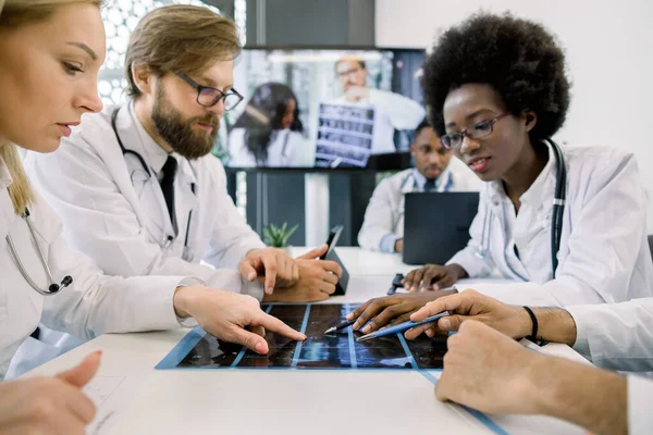 Uluslararası tıp uzmanlarından oluşan bir ekip video konferansında hastaların tomografilerini inceliyor. Genç Afrikalı kadın ve beyaz adam dijital ekranda meslektaşlarına konferans veriyor. — Stok fotoğraf