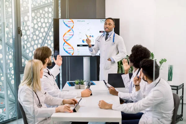 Modern ofisteki masada oturan ve tartışan çok ırklı tıbbi ekip. Yakışıklı Afrikalı doktor modern tıbbın ve yeni biyokimyasal moleküllerin gelişimi hakkında konuşma yapacak. — Stok fotoğraf