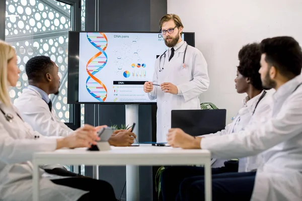 Une équipe de médecins multiethniques en réunion, regardant leur collègue, jeune homme caucasien médecin ou biochimiste, montrant à l'écran quelques formules biochimiques. Médecine, concept scientifique — Photo