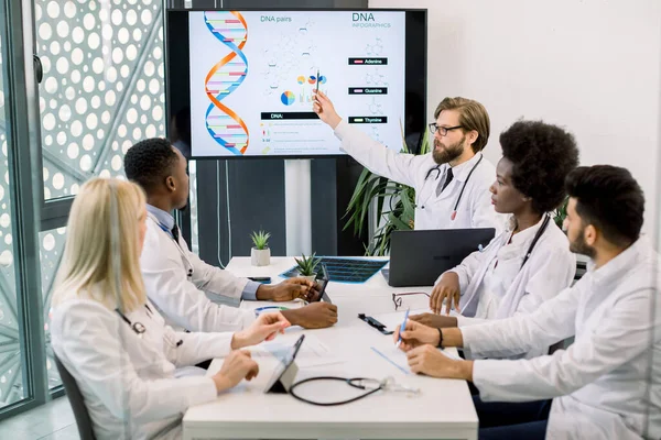Талия портрет многонациональных пяти врачей на совещании медицинского персонала, глядя на цифровой экран, сидя за столом и обсуждая. Белый врач, показывает коллегам карту. — стоковое фото