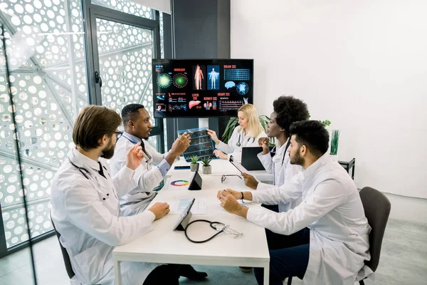 Équipe médicale internationale concentrée ayant une réunion dans la salle de conférence à l'hôpital, discutant et interagissant les uns avec les autres, travaillant avec les patients tomodensitométrie — Photo