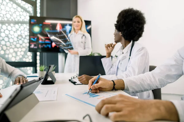 Uluslararası doktorlarla konferans odasında buluşmak, kadın hoparlörleri dinlemek, CT taraması yapmak. Not alan Hintli erkek doktorun ellerine odaklan. Afrikalı kadın hocaya bakıyor — Stok fotoğraf