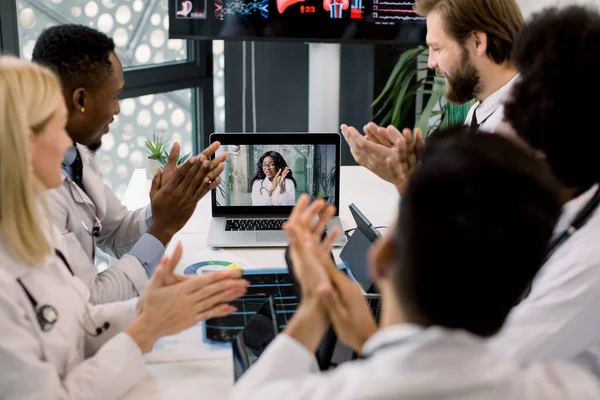 Çevrimiçi video görüşmeleri sırasında çok ırklı doktorlardan oluşan neşeli bir ekip, heyecanlı Afrikalı kadın meslektaşlarının başarılı konuşmalarından sonra el çırpıyorlar. Dizüstü bilgisayardaki siyahi kadına odaklan. — Stok fotoğraf