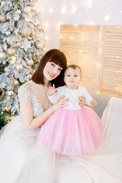 かわいい女の子と若い魅力的な家族、可愛い赤い髪の母親、ソファに座って、装飾されたクリスマスツリーとライトの背景に — ストック写真