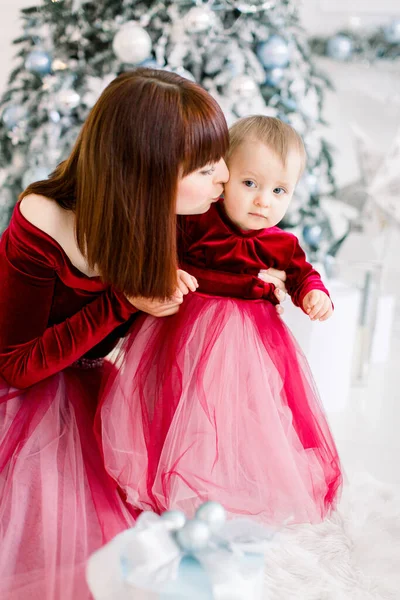 Férias de Natal, conceito de família. Muito jovem mãe beijando sua filha bonita doce pouco, passar o tempo de inverno juntos, sentado no chão na frente da árvore de Natal — Fotografia de Stock