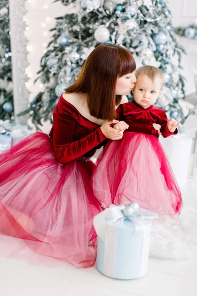 Férias de Natal, conceito de família. Muito jovem mãe beijando sua filha bonita doce pouco, passar o tempo de inverno juntos, sentado no chão na frente da árvore de Natal — Fotografia de Stock