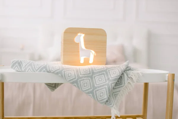 Ahşap gece lambasının önü. Zürafa kesilmiş, gri battaniyenin üstünde, yatak odasının iç tarafında. Evdeki ahşap dekorasyonlar. — Stok fotoğraf