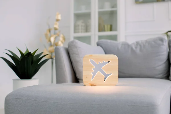 Wooden night lamp with plane picture, on gray monochrome sofa, at stylish light home living room interior. Home decor and lamps. Wooden hand made accessories