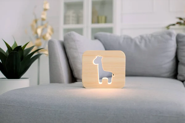 Home decor and lamps. Wooden hand made accessories. Wooden night lamp with giraffe picture, on gray soft comfortable sofa, at stylish light home living room interior.