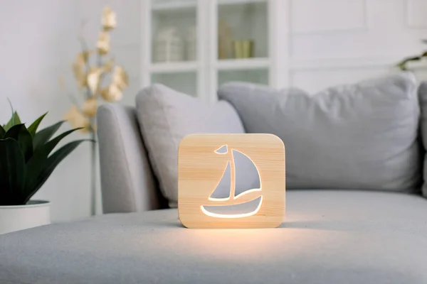 Wooden night lamp with ship picture, on gray stylish sofa, at modern light home living room interior. Home decor and lamps. Wooden hand made accessories