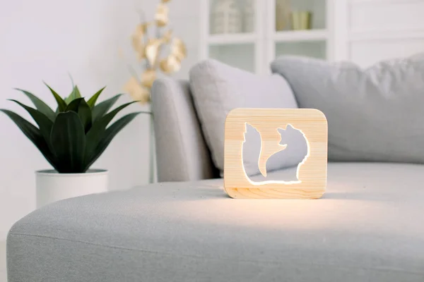 Wooden night lamp with fox cut out picture, on gray monochrome sofa, at stylish light home living room interior. Home decor and lamps. Wooden hand made accessories