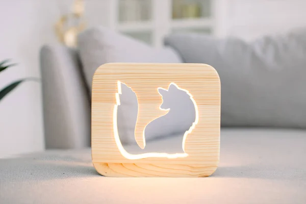 Home decor and accessories, night lamps. Close up of wooden night lamp with fox cut out picture, at stylish light home living room interior, on gray modern sofa.