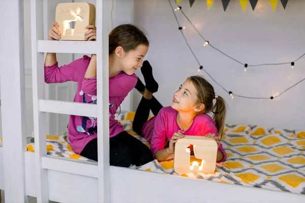 Portret van mooie kinderen, twee kleine mooie meisjes zusjes, spelen met houten nachtlampjes in stijlvol ingericht stapelbed. Kinderen, speelgoed, nachtlampjes, avondconcept — Stockfoto