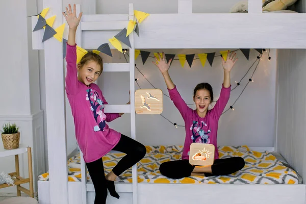 Çocuklar yatak odasında oynuyor. İki komik mutlu kız, 10 yaşında, renkli pijamalı kız kardeşler, ranzada eğleniyorlar, ellerinde tahta gece lambaları var. — Stok fotoğraf