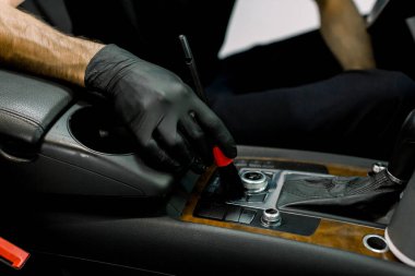 Lastik eldiven giymiş, özel yumuşak fırça kullanarak lüks arabanın içindeki tozları temizleyen erkek araba servis elemanının yakın plan görüntüsü. Araba temizleme ve temizlik konsepti, kuru yıkama.