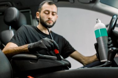 Arabanın içi plastik bakım, detay konsepti. Beyaz tenli erkek otomobil tamircisinin portresi, içi yumuşak fırça ve özel profesyonel bakım sütüyle temizlenmiş araba. Eline odaklan.