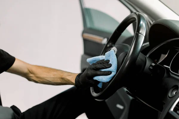Detailní série aut, koncepce mytí a čištění automobilů. Oříznuté zblízka obraz ruky mužského pracovníka v černé ochranné rukavici, čištění volantu auta s modrým mikrovláknitým oblečením — Stock fotografie