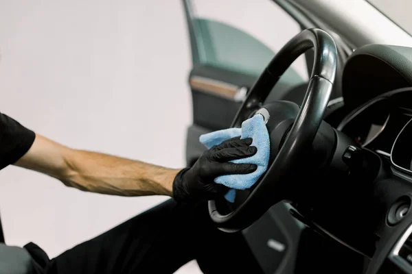 Carro detalhando série, lavagem de carro e conceito de limpeza. Cortado de perto imagem da mão do trabalhador masculino em luva protetora preta, limpando o volante do carro com roupas de microfibra azul — Fotografia de Stock