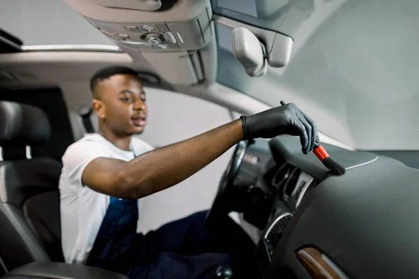 차 자세 한 것은 플라스틱 관리 개념입니다. 차 내부에 있는 먼지를 닦아 내고 통제 패널이야. 젊은 아프리카 남자가 차 내부와 앞 패널을 붓으로 청소 합니다. 손에 초점을 맞춘 선택 — 스톡 사진