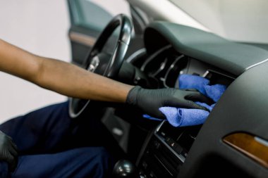 Mavi mikrofiber bez, arabanın içini ve ön plastik paneli tozdan temizleyen Afrikalı erkek otopsi işçisinin elini kapatın. Araba temizliği, dezenfeksiyon, vale konsepti