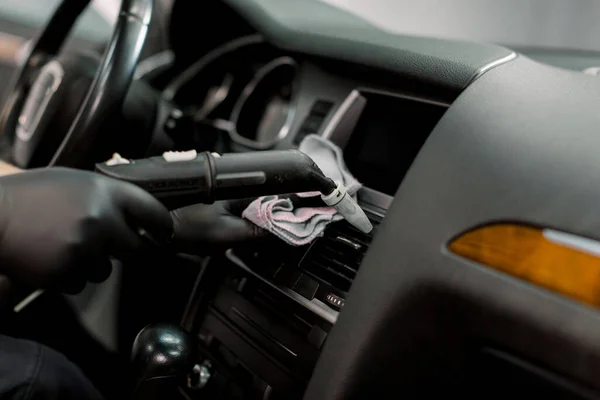 Cleaning of car air duct with hot steam cleaner. Steam heat cleaning, disinfection of vehicles. Close up cropped shot of hands of male worker, cleaning car interior with hot steam and cloth