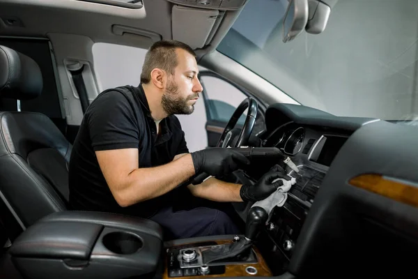 Limpeza de serviço de ar condicionado do carro com vapor quente. Trabalhador masculino caucasiano profissional concentrado em uniforme preto, sentado no banco da frente do carro moderno e usando limpador de vapor quente — Fotografia de Stock