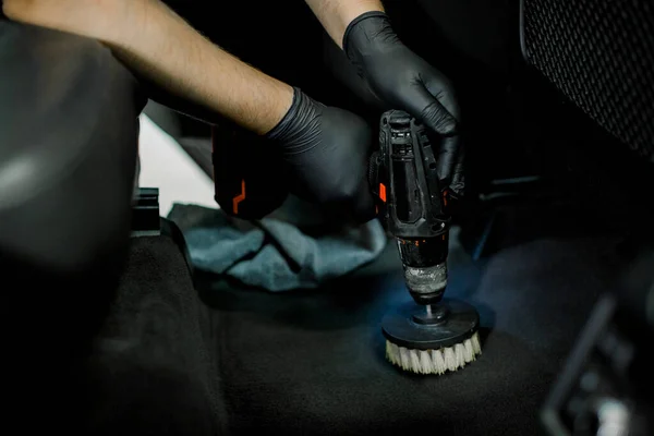 Close up cropped image of male hands in protective gloves, cleaning car interior and floor by chemical foam and scrubbing machine, electric brush. Car detailing and wash concept — Stock Photo, Image