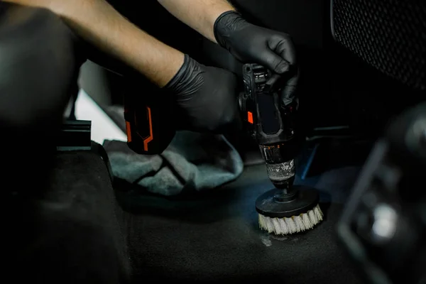 Close up cropped image of male hands in protective gloves, cleaning car interior and floor by chemical foam and scrubbing machine, electric brush. Car detailing and wash concept — Fotografia de Stock