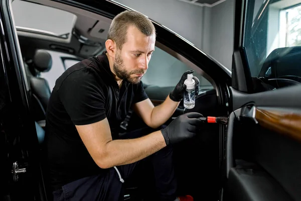 Jovem carro bonito detalhando trabalhador fazendo limpeza profissional e remoção da poeira do interior do carro, usando limpeza especial desinfectando espuma e escova macia. Limpeza interior do carro — Fotografia de Stock