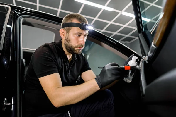 Trabalhador de serviço automóvel masculino profissional em luvas uniformes e protetoras pretas, realiza uma limpeza da porta do veículo moderno com espuma de limpeza e escova macia — Fotografia de Stock