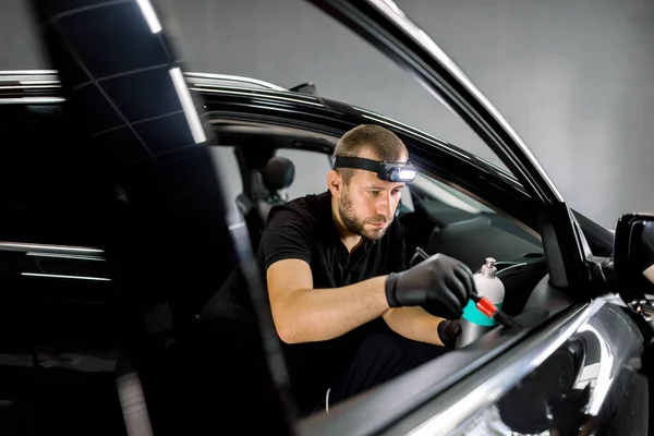 Ung automatisk bensinstation manliga arbetare, bär uniform och handskar, gör rengöring och skötsel förfarande för läder och plast delar av bildörren interiör, med hjälp av borste och speciell mjölk — Stockfoto