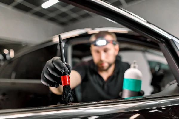 Close-up de homem, trabalhador da estação de serviço de carro, fazendo procedimentos de limpeza e cuidados para o interior da porta do carro, usando escova e creme especial ou leite para cuidados de couro e remoção de arranhões. Foco na mão — Fotografia de Stock