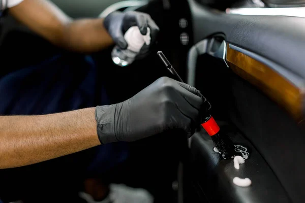 Close up de mãos de trabalhador de serviços de lavagem de carros de pele escura em luvas de proteção pretas, limpeza da porta do carro com espuma especial de desinfecção química e escova macia. Lavagem de carro, detalhamento e desinfecção — Fotografia de Stock