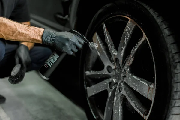 Mytí auta ručně, detaily auta. Oříznutý obraz rukou mladého muže v ochranných rukavicích postřikující speciální čisticí roztok na okraj moderního vozidla na mytí aut — Stock fotografie