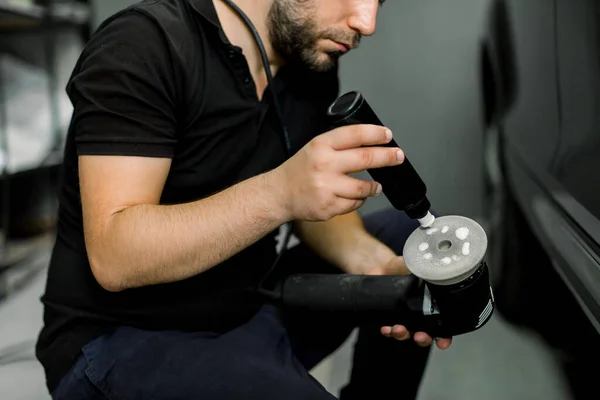 Beskuren bild av händerna på manliga auto servicearbetare, tillämpa speciella polervax eller grädde på omloppsbanan polermaskin för att polera bilen på bakgrunden. Bildetaljer och polering koncept — Stockfoto