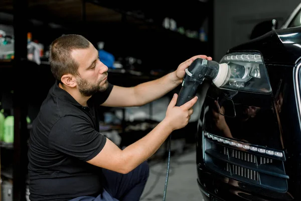 Närbild av professionell kaukasiska manliga auto servicearbetare, vaxning och polering strålkastare svart bil med omloppsbana polerare. Bildetalj serie, polering koncept. — Stockfoto