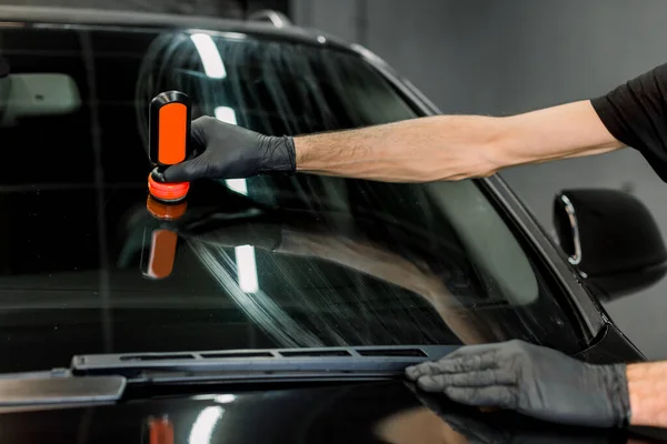 Zamknij przycięty obraz męskiej dłoni w rękawiczce ochronnej, stosując skład antydeszczowy dla szyby samochodowej. mężczyzna ręka i samochód szyba przednia zbliżenie — Zdjęcie stockowe