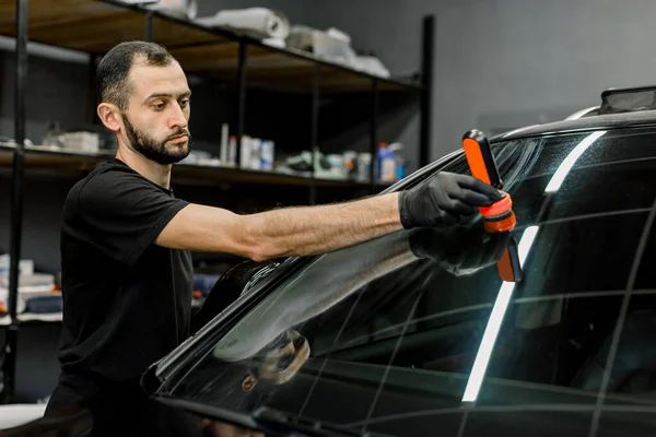 Stilig ung manlig arbetare av auto detalj tvättservice, beläggning bil vindruta och fönster med professionell anti regn sammansättning. Selektivt fokus på ansiktet — Stockfoto