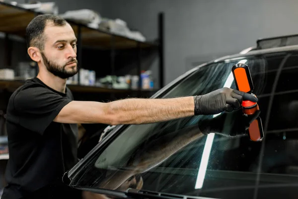 Stilig ung manlig arbetare av auto detalj tvättservice, beläggning bil vindruta och fönster med professionell anti regn sammansättning. Selektivt fokus på hand — Stockfoto