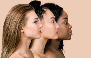 Üç güzel çok kültürlü genç kadının profil portresi. Stüdyoda bej arka planda poz veren Avrupalı, Asyalı ve Afrikalı kadınların yüzlerini kapatın. Etnik ten tipleri. Farklı etnik köken