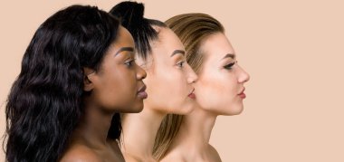 Çeşitlilik, çok ırklı güzellik kavramı. Farklı ırklardan üç güzel bayan, Afrikalı, Asyalı ve Kafkasyalı, doğal makyajlı, bej renkli stüdyo arka planında poz veren, sıra sıra bekleyen