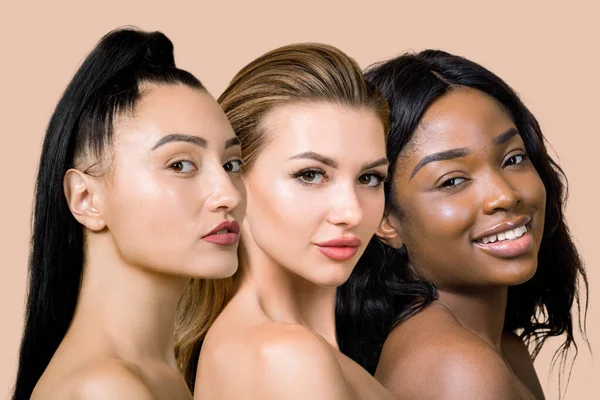 Close up retrato de colagem de beleza de três jovens modelos femininos multirraciais com ombros nus e bela pele pura, olhando para a câmera, no fundo do estúdio bege claro. Beleza mundial — Fotografia de Stock