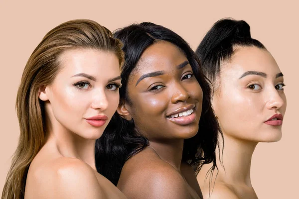 Spa and natural beauty, skincare promotion. Three attractive diverse ladies, European, African and Asian, posing to camera face to face, on isolated beige background. Collage beauty shot — Stock Photo, Image
